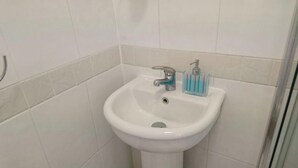 Een badkamer met een wit wastafeltje, een kraan en een zeepdispenser.