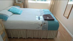 Een bed met een wit-turquoise dekbedovertrek, een bruine handdoek en een afstandsbediening op het bed.