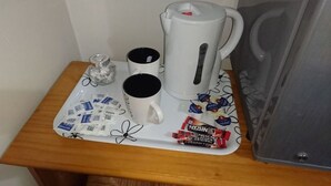 Een dienblad met twee witte mokken, een witte elektrische waterkoker en enkele chocoladerepen op een houten tafel.