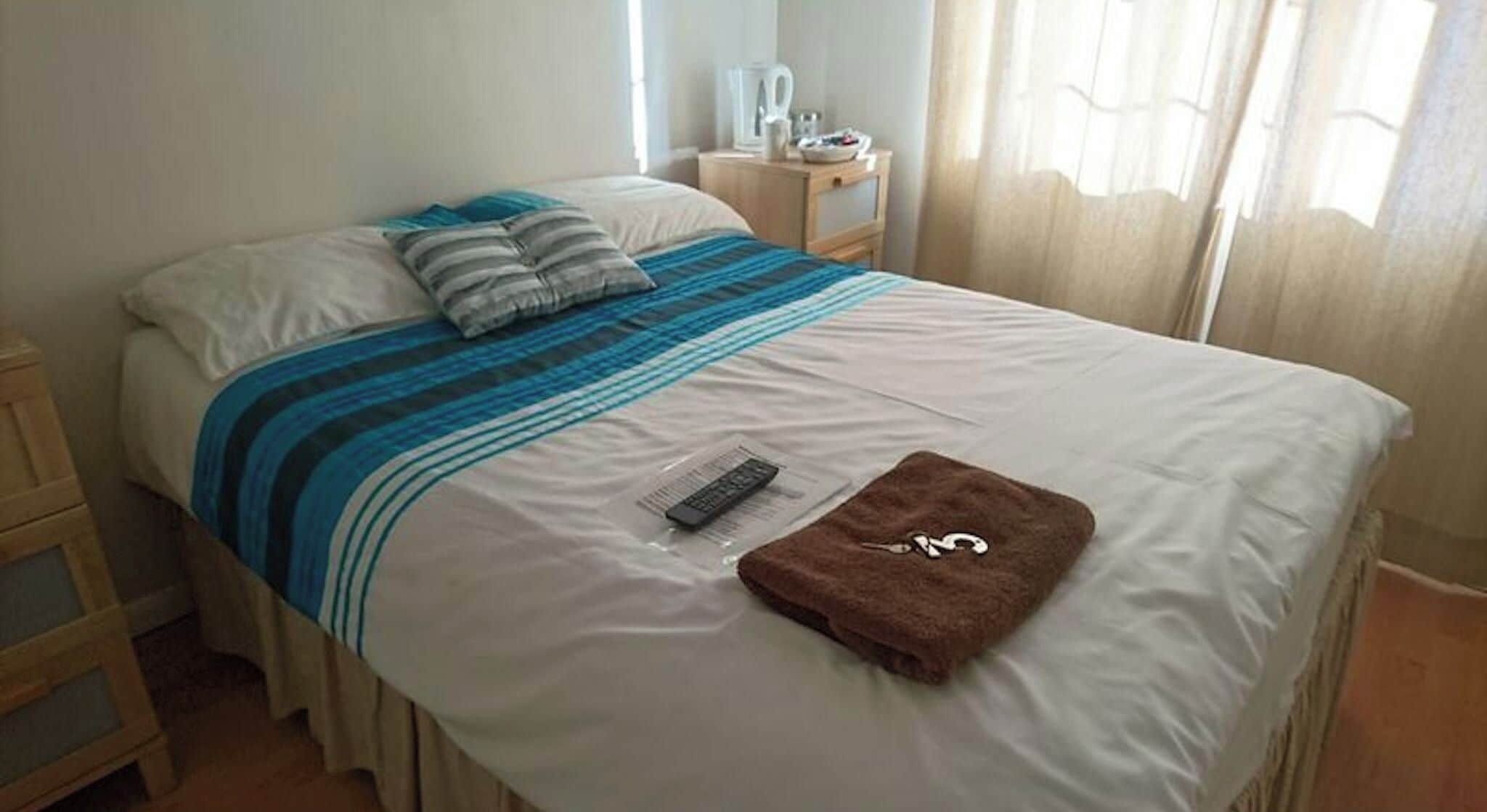 Una cama bien hecha con una colcha a rayas, un control remoto y una toalla marrón encima.