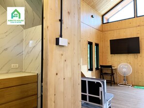 Interior de madera con un banco empotrado, un televisor montado en la pared y un ventilador de pie.
