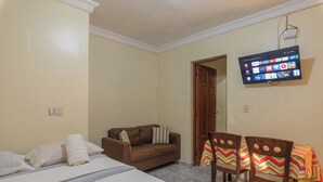 Een hotelkamer met een bed, een slaapbank, een aan de muur bevestigde televisie en een tafel met stoelen.