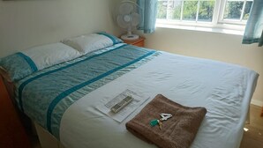 Una cama bien tendida con una colcha azul y blanca, un control remoto, un llavero y un papel sobre la cama.
