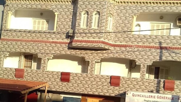 A multi-story building with a brick facade, a covered entrance, and a sign for a general hardware store. - Room-dar el Baraka - Banzart (Bizerte)
