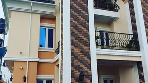 Un edificio residencial de varios pisos con un balcón en el segundo piso, una puerta de garaje visible y cielo despejado.