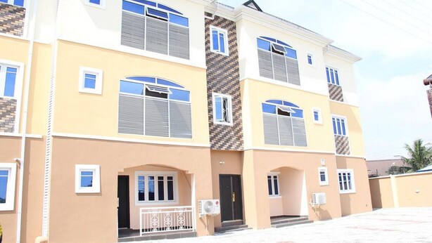 A multi-story residential building with a beige facade, multiple windows, and a central entrance with a small porch. - Room-blooms Spot Hotel -guest Room (Port Harcourt)
