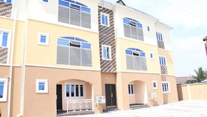 Un edificio residenziale a più piani con facciata beige, numerose finestre e un ingresso centrale con un piccolo portico.