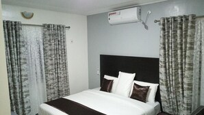 Una camera d'albergo con un letto, tende, un comodino e un condizionatore d'aria.