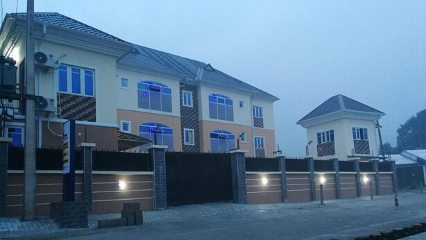 Un edificio residenziale a più piani con cancello, vialetto e una piccola costruzione adiacente.
