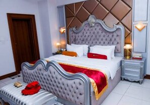 Een slaapkamer met een geborduurde hoofdbord, een bed met wit en rood beddengoed, een nachtkastje met een lamp, en een nachtkastje.