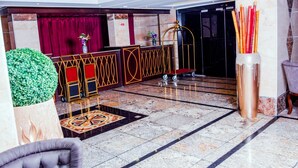 A lobby with a reception desk, a green decorative plant, a patterned carpet, and a large vase with pencils. - Room-limewood Hotel - Guest Room (Port Harcourt)