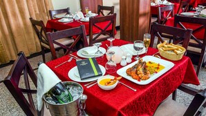 A dining table set with a red tablecloth, a lobster dish, a basket of bread, and a wine glass. - Room-limewood Hotel - Guest Room (Port Harcourt)