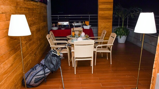 A dining area with a table set for four, surrounded by wicker chairs, a red tablecloth, and a grill in the background. - Room-limewood Hotel - Guest Room (Port Harcourt)