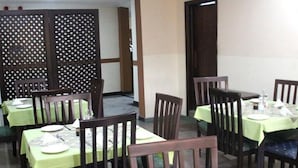 A dining area with tables set for four, each with a green tablecloth and wooden chairs. - Room-the Golf Prince Hotel-guest Room (Port Harcourt)