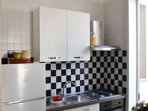 Eine Küche mit weißen Schränken, einer schwarz-weißen Schachbrettfliesenrückwand, einer Edelstahl-Spüle und einem Gasherd.