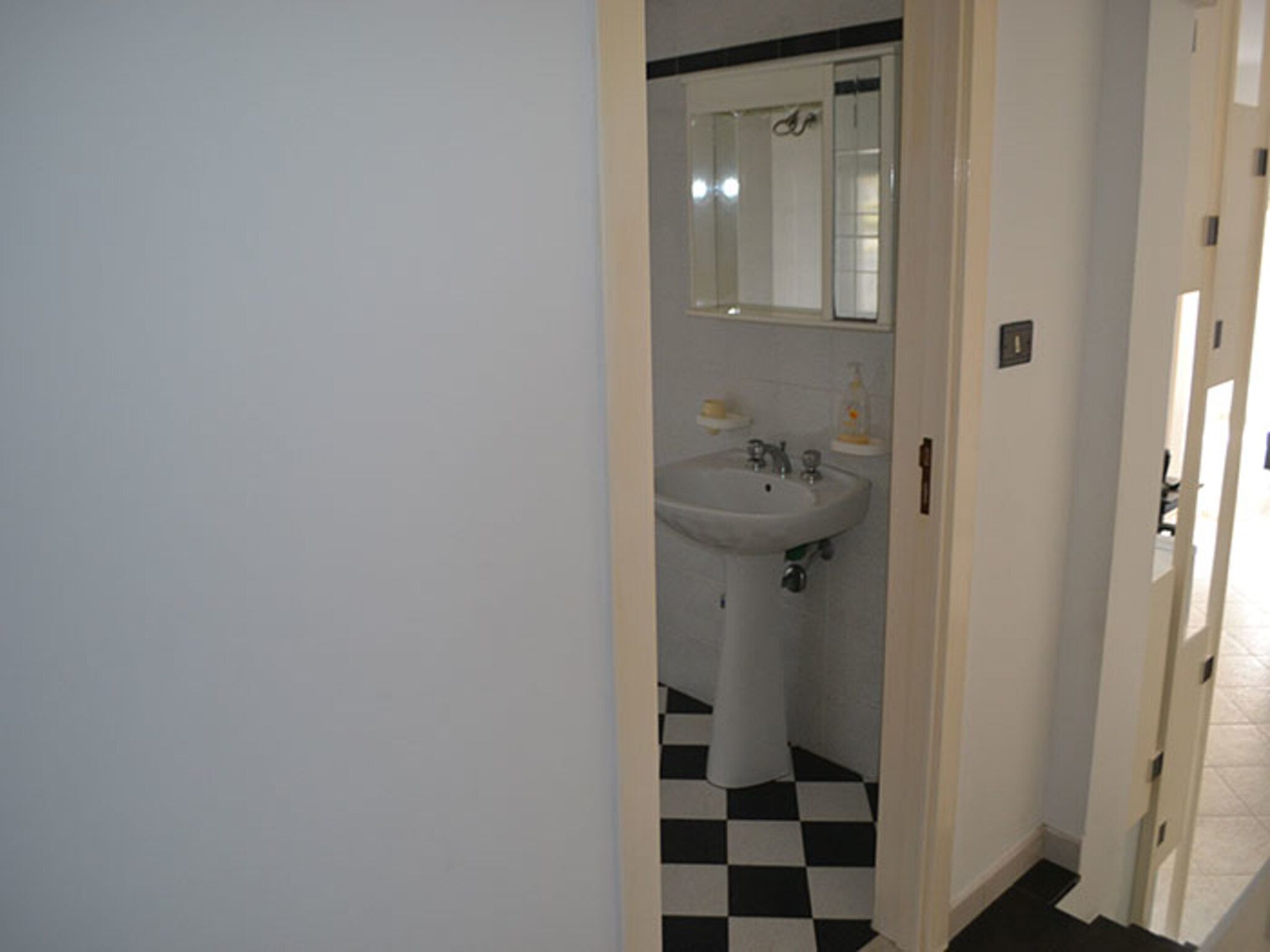 A bathroom with a white sink, mirror, and black-and-white checkered floor.