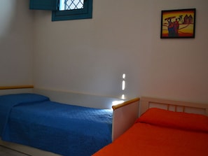 Quarto com duas camas de solteiro, uma com colcha azul e outra com colcha laranja.