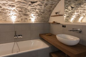 A modern bathroom with a stone wall, a white bathtub, a wooden vanity, and a large mirror.