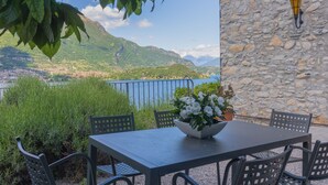 A table with chairs and a potted plant, overlooking a scenic view of mountains and a body of water. - The Amazing Villa Claudia Tuscany Style (Lezzeno)