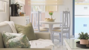 Ein modernes Wohnzimmer mit einer Couch, einem Esstisch und Stühlen. Auf dem Tisch steht eine Kaffeemaschine und nebenan eine Pflanze.