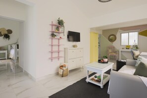 A modern living room with a white sofa, a glass coffee table, a pink shelving unit with plants, a flat-screen TV, and a yellow accent wall. - Unwind and Recharge in This Homey Central Retreat (Punta Cana)