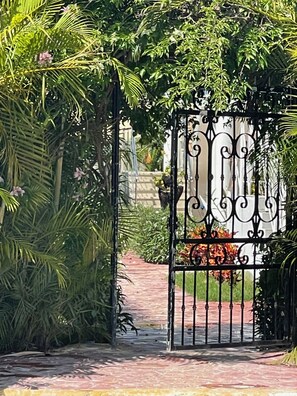 A wrought iron gate with intricate designs, leading to a pathway surrounded by lush greenery and potted plants. - Unwind and Recharge in This Homey Central Retreat (Punta Cana)