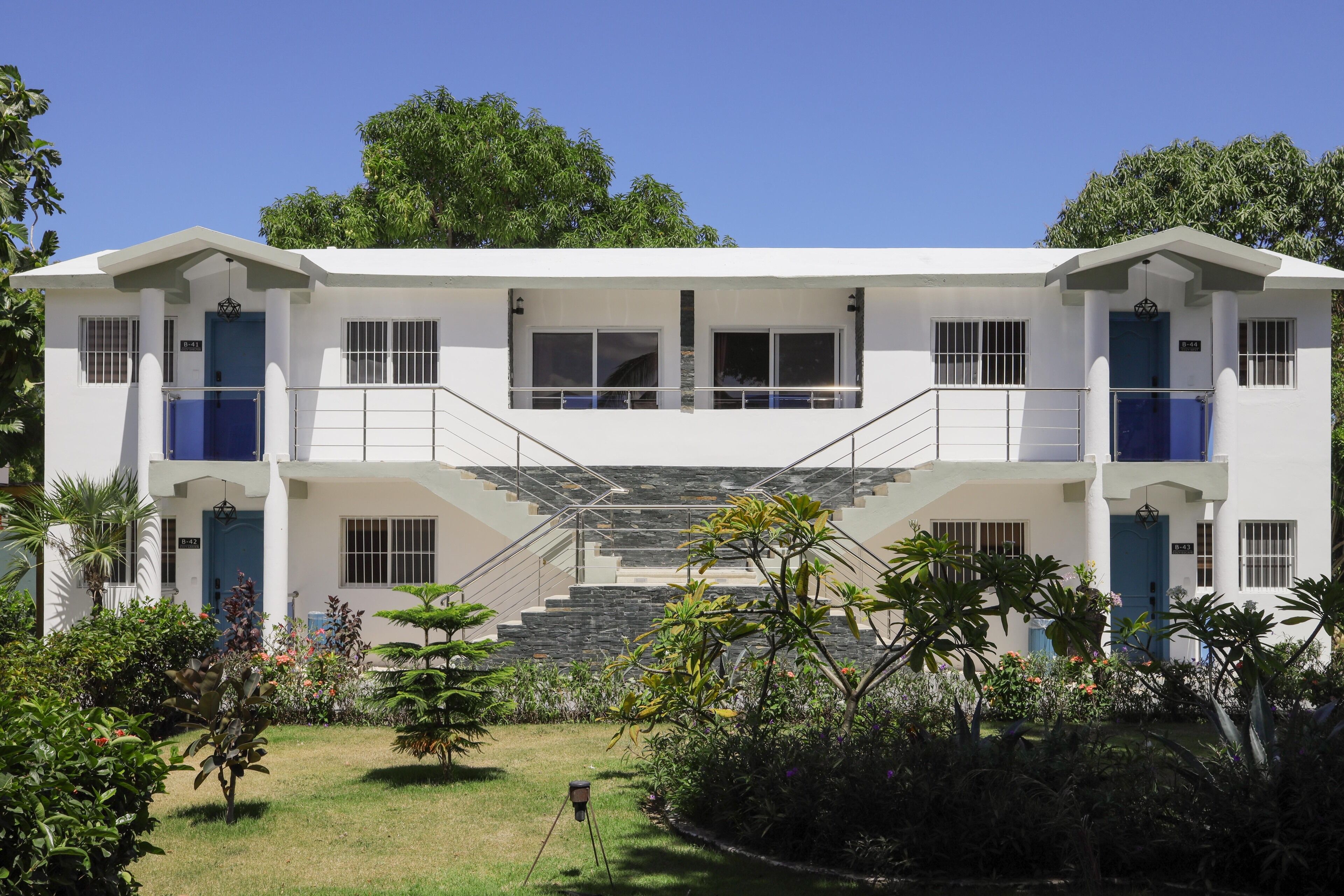 A two-story building with a central staircase, multiple windows, and a well-maintained garden with various plants and flowers.