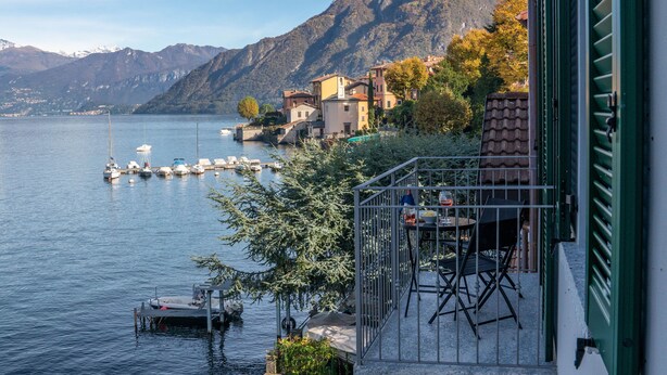 Ein Anwesen am Seeufer mit Terrasse, Liegeplätzen für Boote und Bergen im Hintergrund.