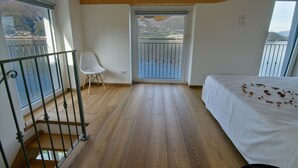 Ein Schlafzimmer mit Holzboden, einem Bett, einem Sessel und einem Balkon mit Blick auf das Wasser.