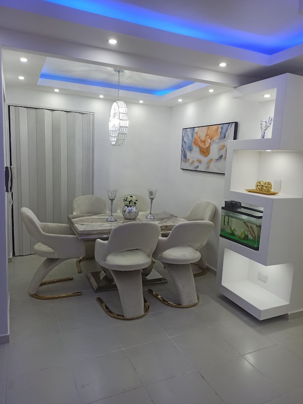 A modern dining area with a white table, four chairs, and a fish tank on a white shelf.
