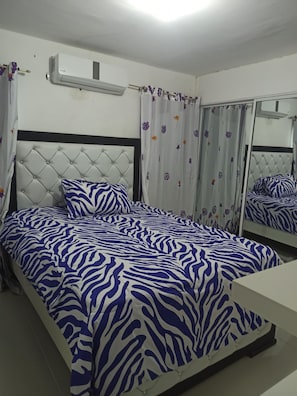 A bedroom with a bed featuring a zebra-patterned bedspread, a tufted headboard, and a mirror on the wall.