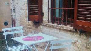 A white metal table and chairs set outside a building with a stone wall and wooden shutters. - Casa Sara Holiday Home (Spello)