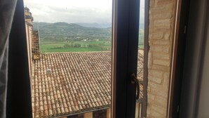 A view from a window with a tiled roof, overlooking a green landscape with hills and a few buildings. - Casa Sara Holiday Home (Spello)
