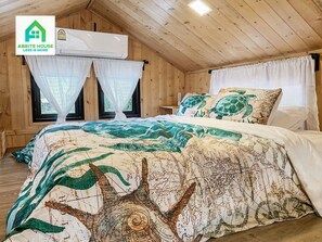 A cozy room with wooden walls, a bed with a patterned bedspread, two windows with sheer curtains, and an air conditioning unit. - Tiny House on Koh Lanta Only 2 Minutes Walk to the Beach (Ko Lanta)