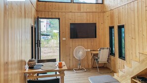 En inredning med träpaneler, ett matområde, en tv som är monterad på väggen och ett stort fönster som släpper in naturligt ljus.
