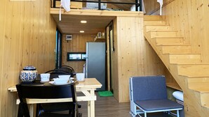 Una cabaña de madera compacta con un dormitorio en el altillo, una kitchenette y un comedor.