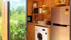 Cocina compacta con armarios de madera, lavadora, refrigerador Samsung y ventana con vista a zonas verdes.