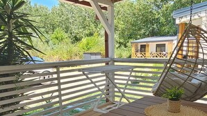 Una terraza cubierta al aire libre con una mesa y sillas, un sillón colgante y vistas a una casa y follaje.