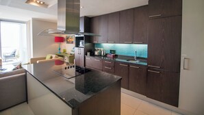 A modern kitchen with dark wood cabinets, a granite countertop, and a stainless steel range hood. - Camps Bay One Bedroom Apartment - The Crystal (Cape Town)
