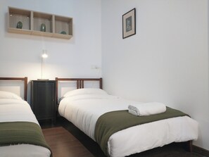 A simple, clean room with two single beds, a bedside table, a lamp, and a shelf with decorative items. - Lovely Flat In Barceloneta Near Sea (Barcelona)