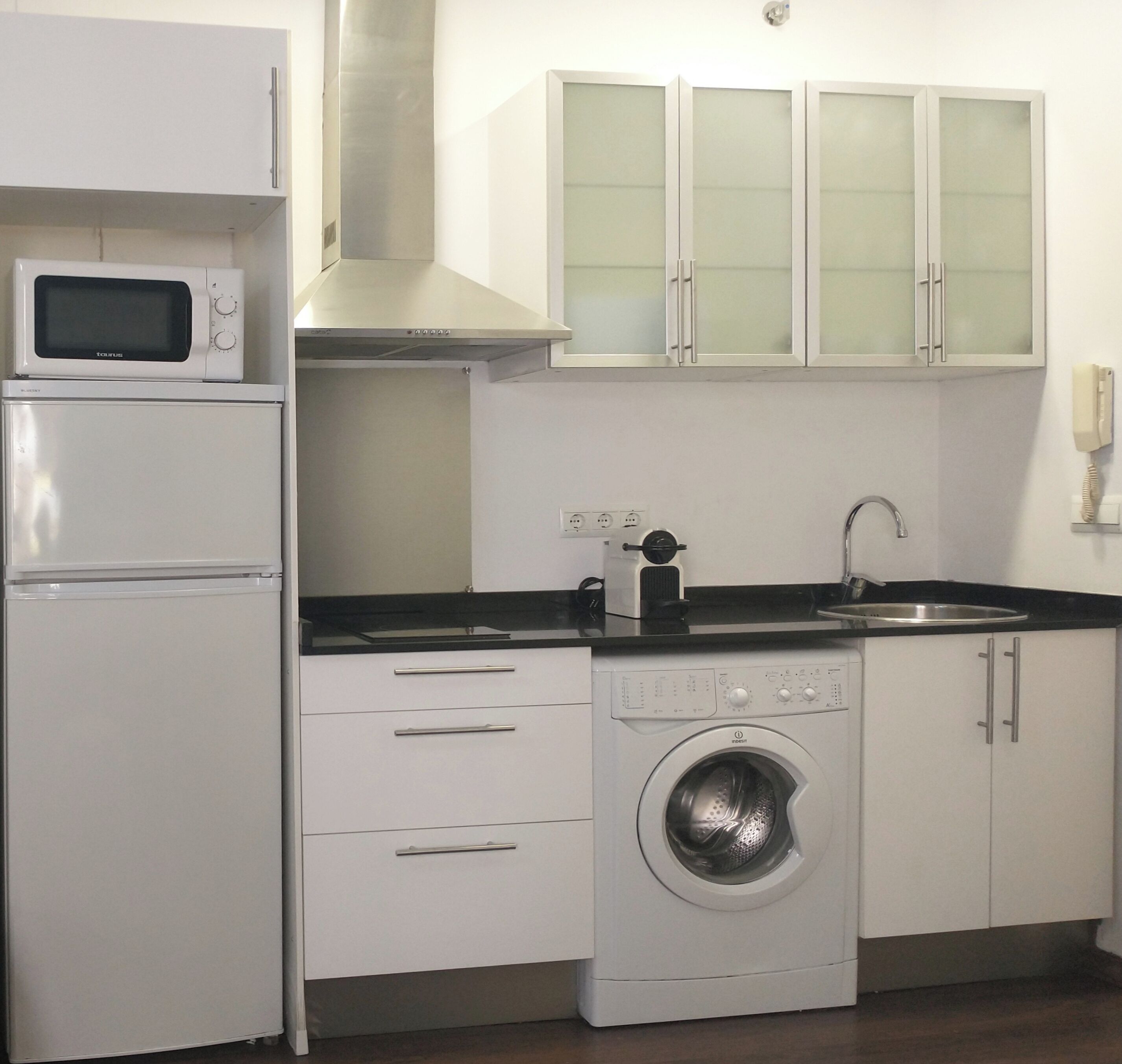 A compact kitchen with a microwave, oven, washing machine, and a sink.