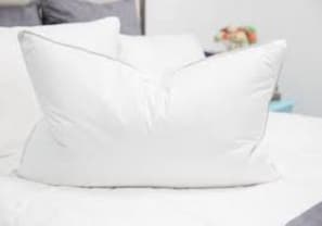 A white pillow on a bed with a white headboard.