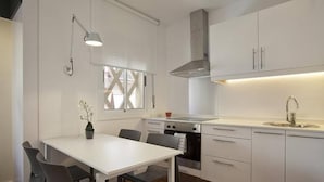 A modern kitchen with white cabinetry, a dining table with chairs, a built-in oven, and a window with cross-bracing.