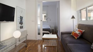 A compact living space with a bed, a sofa, a small table, a TV, and a window.