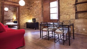 Een rustieke kamer met stenen muren, een houten plafond, een glazen tafel met stoelen, een rode bank en een televisie op een zwarte kast.