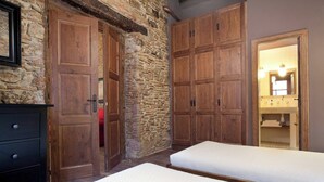 Een slaapkamer met twee bedden, houten kasten, een stenen muur en een badkamer die door een open deur zichtbaar is.