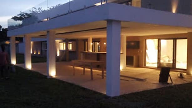 Une maison moderne dotée d’un patio couvert, de grandes fenêtres et d’un intérieur bien éclairé.