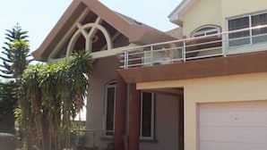 Une maison à deux étages avec un balcon, un garage et un grand arbre au premier plan.