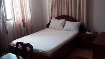 A single bed with white bedding, a wooden headboard, and a nightstand with a lamp.