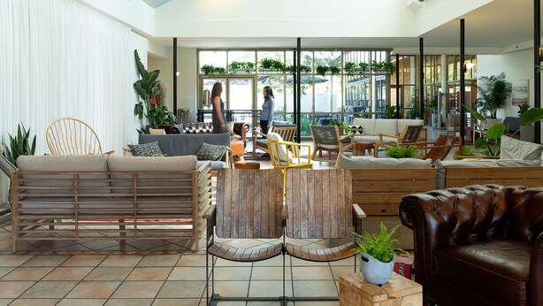 A spacious indoor area with a variety of seating options, including sofas, chairs, and a wooden bench. There are large windows providing natural light and views of the outdoors. - Shefayim Hotel (Hod HaSharon)